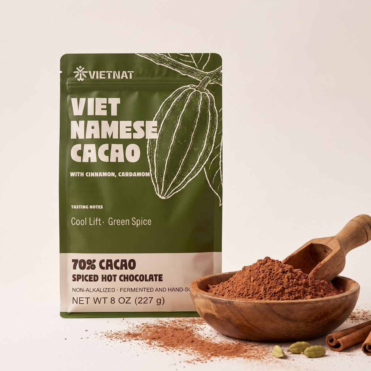 Fine cacao and spice grind in a wooden bowl beside the pouch, with cinnamon quills and green cardamom pods