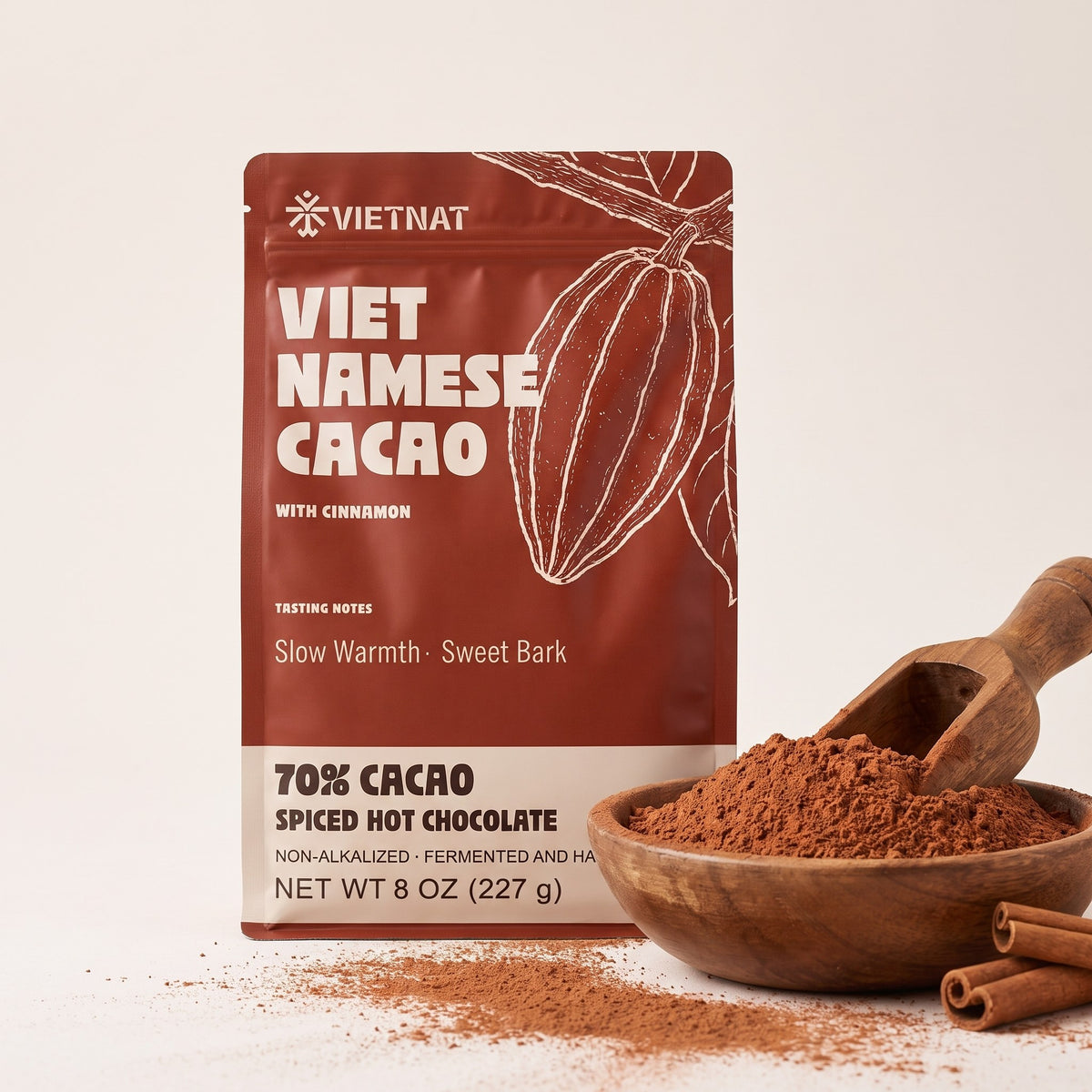 Fine cacao and cinnamon grind in a wooden bowl beside the pouch, with cinnamon quills